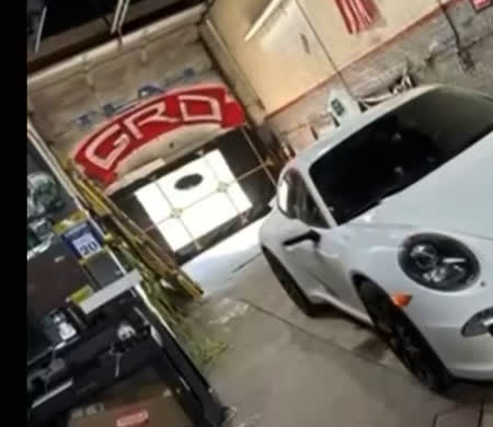White Porsche with tinted windows inside the GRD Creations llc shop, GRD logo on the wall